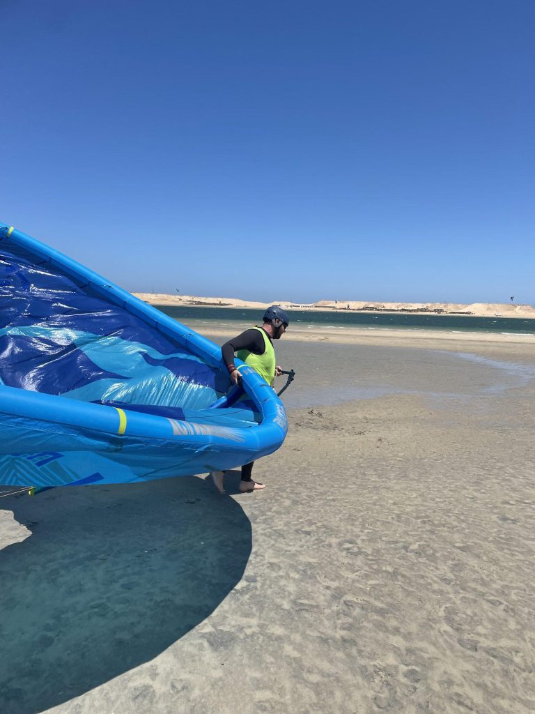 Un kitesurfeur transporte son aile de kitesurf à la main lors d'un cours de kitesurf sur le spot de Dakhla