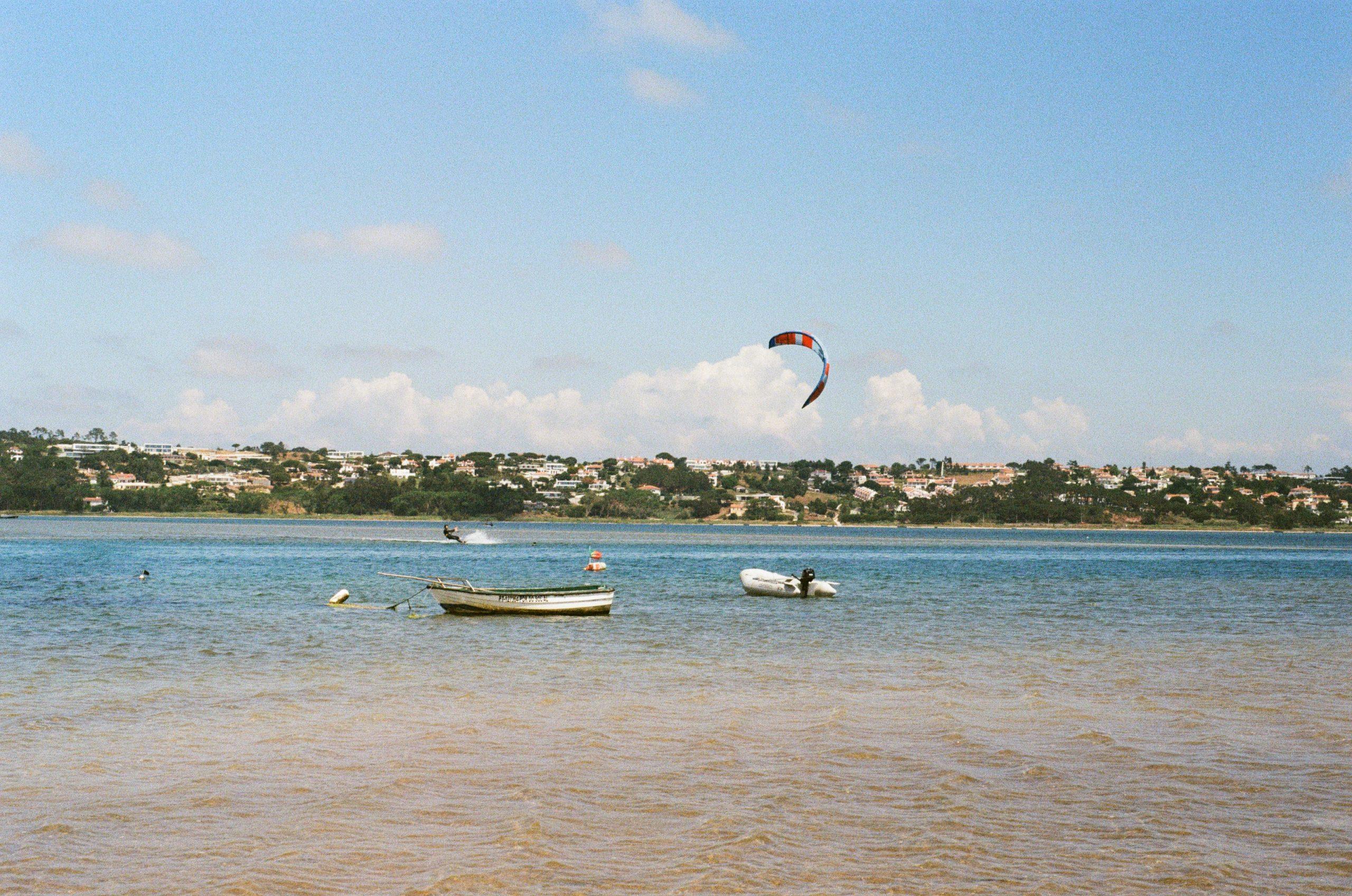 Photo argentique de la lagune d'obidos. Un kitesurfeur navigue sur le spot, deux petites embarcations sont devant lui.