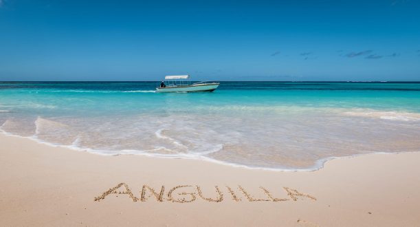 Turquoise sea and white sandy beach of Anguilla, Caribbean. Motorboat passing by. Blue sky on a perfect summer day. Anguilla word written in white soft beach sand.